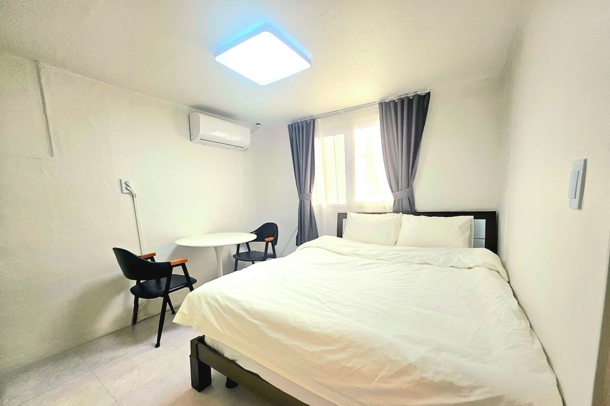 Habitación de hotel con cama, una mesita pequeña con dos sillas, una lámpara de techo y un equipo de aire acondicionado.