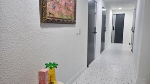 A hallway with white walls, a textured floor, and a painting above a door. - Daldal Masil (Mokpo)