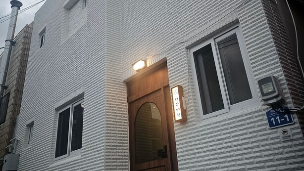 A multi-story building with a textured facade, a wooden door, and a small awning. - Daldal Masil (Mokpo)