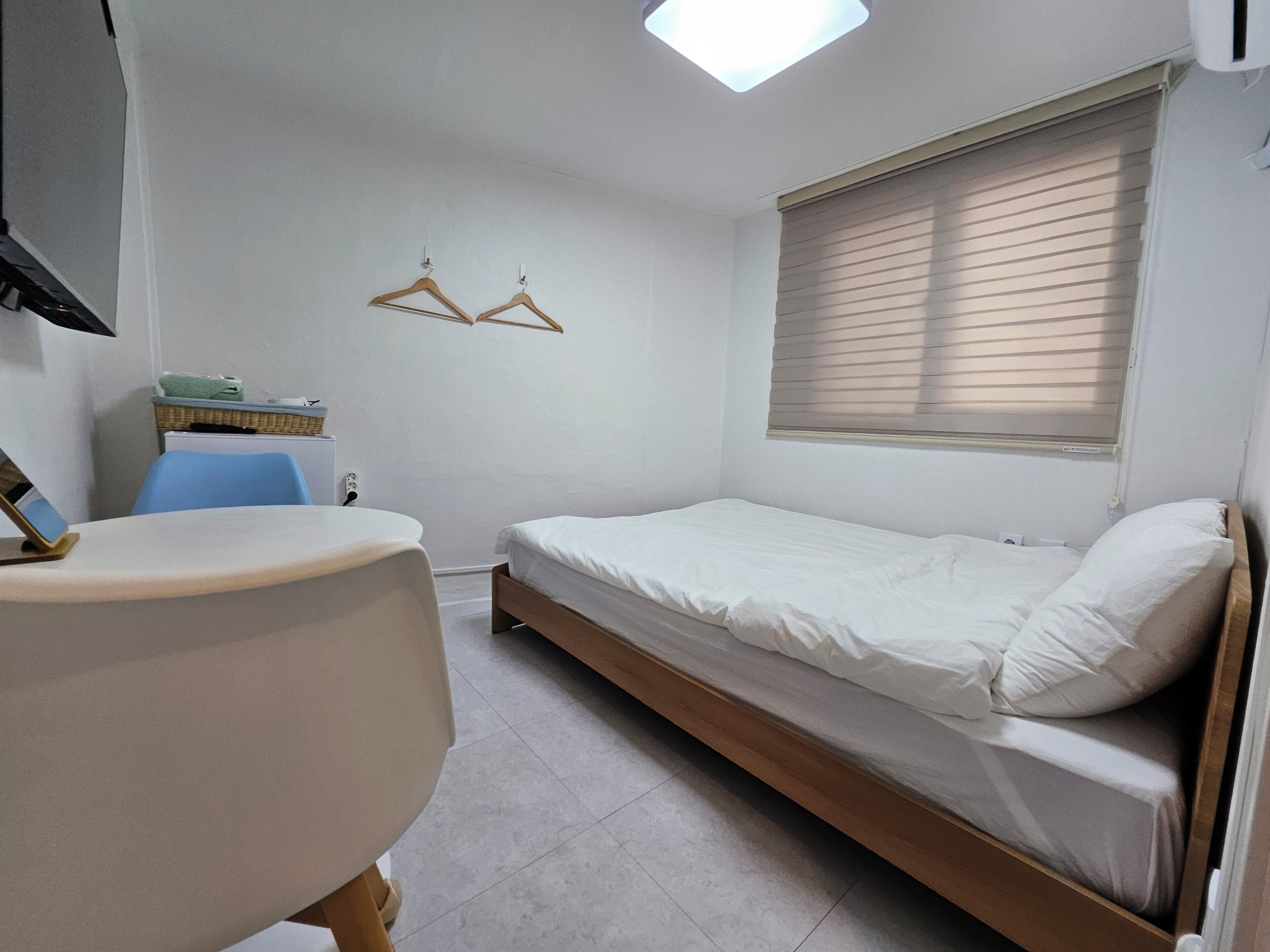 Quarto pequeno e limpo com uma cama de solteiro, uma escrivaninha e uma cadeira.