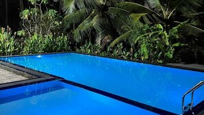 A swimming pool with a clear blue water surface, surrounded by lush greenery and palm trees. - Larala Villa With Private Pool (Hikkaduwa)