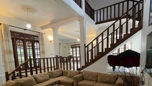 A spacious living room with a large L-shaped sectional sofa, a glass coffee table, and a staircase leading to an upper floor. - Larala Villa With Private Pool (Hikkaduwa)