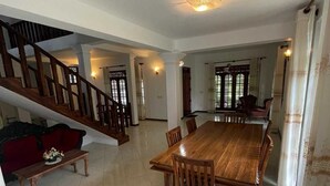 A spacious dining area with a large wooden table and chairs, a staircase, and a red sofa. - Larala Villa With Private Pool (Hikkaduwa)