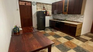 A compact kitchen with dark wooden cabinets, a tiled floor, and a dining table. - Larala Villa With Private Pool (Hikkaduwa)