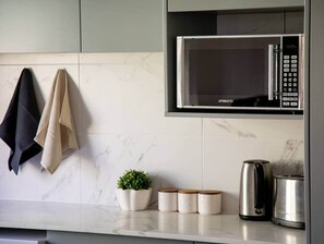 A kitchen with a microwave, a kettle, and a coffee maker. There are towels hanging on a rack and a small potted plant on the counter.