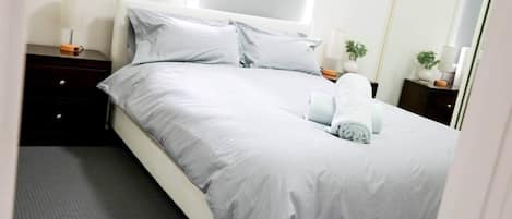 A neatly made bed with a grey bedspread and pillows, a bedside table with a lamp, and a small potted plant on the nightstand.