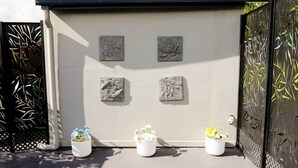 A building with four stone reliefs on the wall, three potted plants in front, and a metal gate with decorative patterns. - Modern Home - 2 min To CBD - Near Lakes & Forests (Oberon)