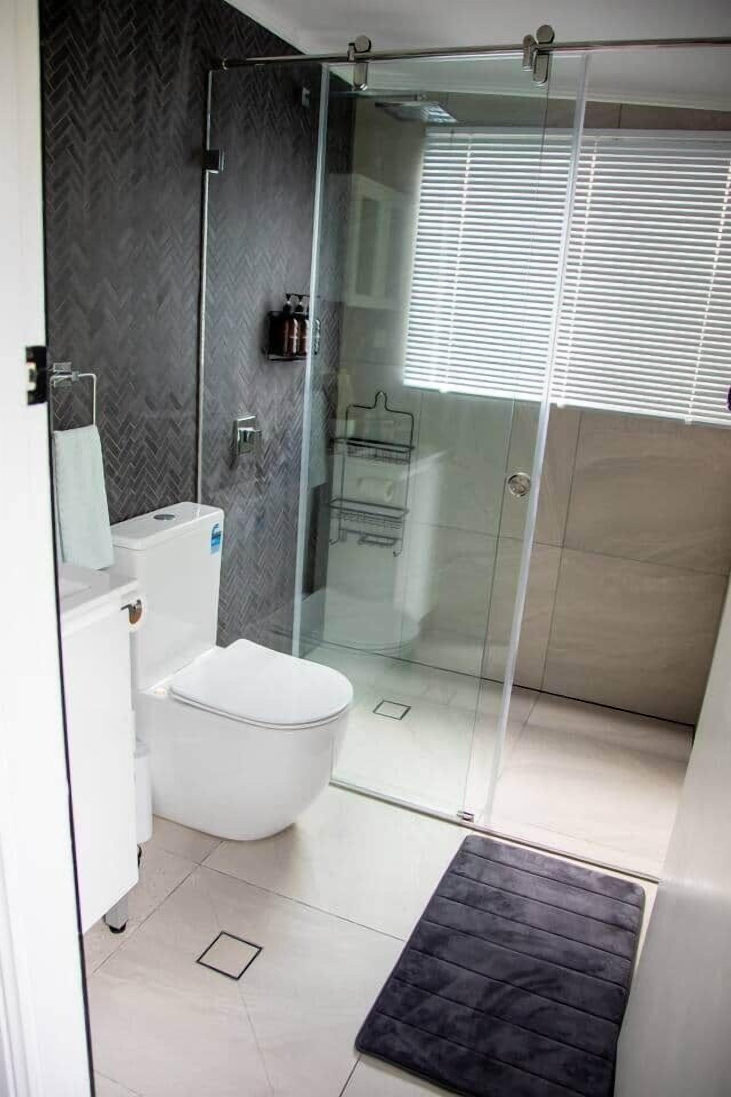 A modern bathroom with a glass shower enclosure, a white toilet, and a herringbone-patterned wall.