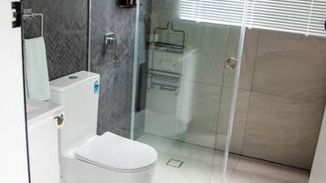 A modern bathroom with a glass shower enclosure, a white toilet, and a herringbone-patterned wall.