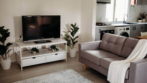 A living room with a flat-screen TV on a white stand, a grey sofa, and a white rug. - Modern Home - 2 min To CBD - Near Lakes & Forests (Oberon)