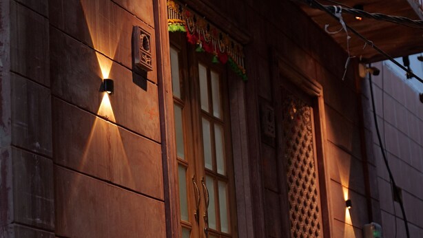 A wooden building with a balcony, a decorative door, and two wall-mounted lights. - Fort View (Jodhpur)