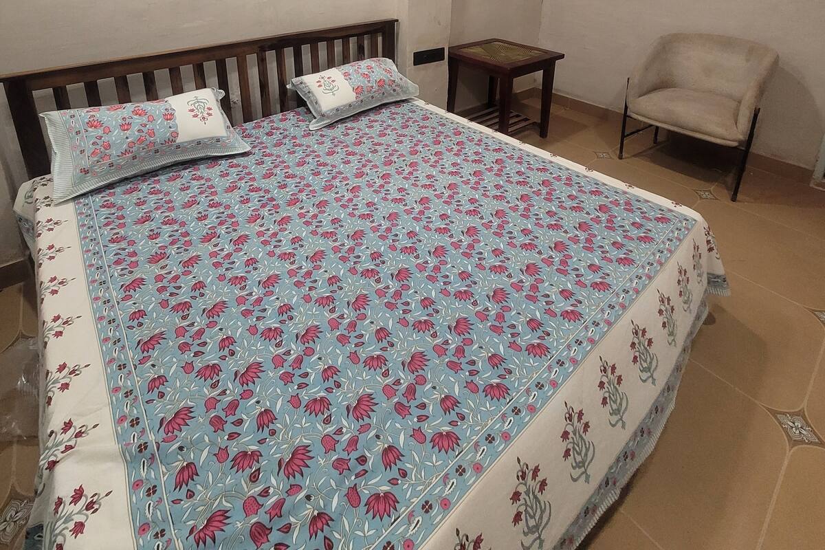 A bedroom with a large bed, two wall-mounted lights, a chair, and a small table.