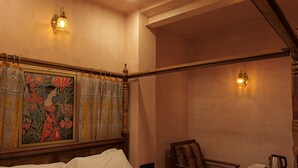 A hotel room with a bed, a chair, a painting, and two wall sconces. - Fort View (Jodhpur)