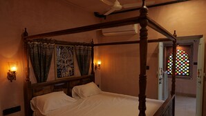 A four-poster bed with a wooden frame and white linens, a ceiling fan, and wall-mounted lamps. - Fort View (Jodhpur)