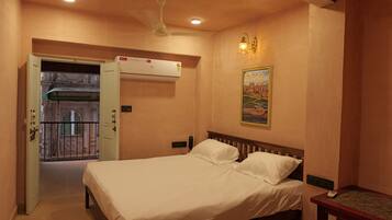 A bedroom with a bed, an air conditioner, a painting, and a door leading to a balcony.