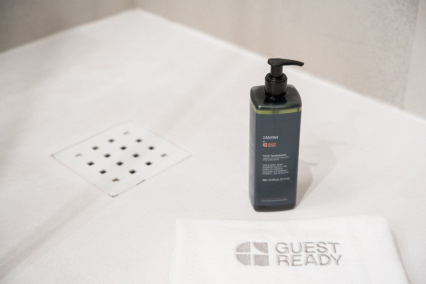 A black bottle of Anyah hair and body wash on a white surface with a drain and a white towel with the text 'GUEST READY'.
