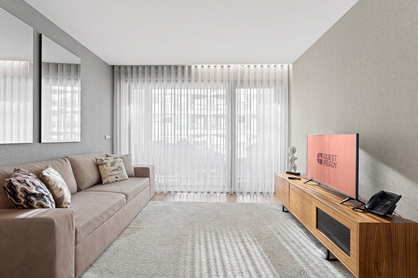 A modern living room with a sofa, a wooden side table, a mirror, and a 'GUEST READY' sign.