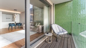 Uma sala de estar moderna com uma porta de vidro que dá para uma varanda, uma área de jantar com cadeiras azuis e uma parede revestida com azulejos verdes.
