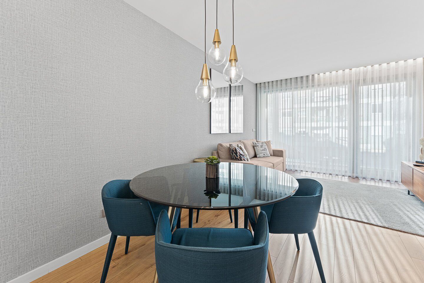 Een moderne eetruimte met een ronde glazen tafel, blauwe bekleden stoelen en een minimalistisch design.