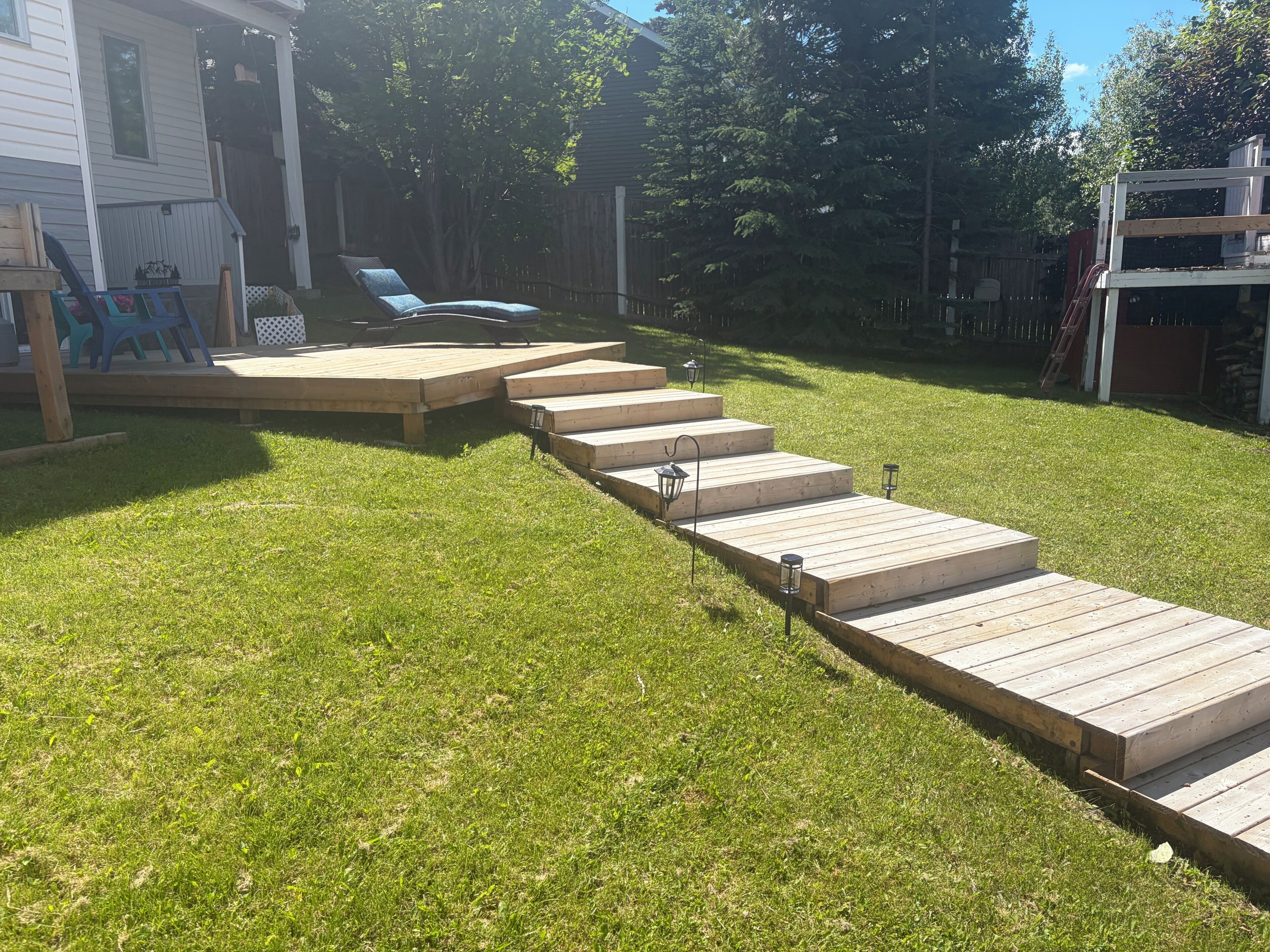 A wooden deck with steps leading to a lawn area, surrounded by a wooden fence and trees.