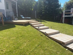 A wooden deck with steps leading to a lawn area, surrounded by a wooden fence and trees. - Hinton Mountain House (Hinton)