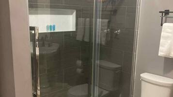 A modern bathroom with a glass-enclosed shower, a toilet, and a white sink.