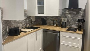 A modern kitchen with white cabinets, a stainless steel dishwasher, a coffee maker, and a knife block. - Hinton Mountain House (Hinton)