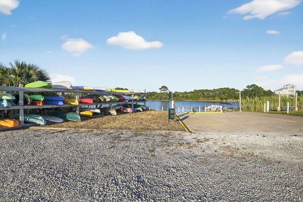 A gravel area with a row of colorful kayaks and a body of water in the background.