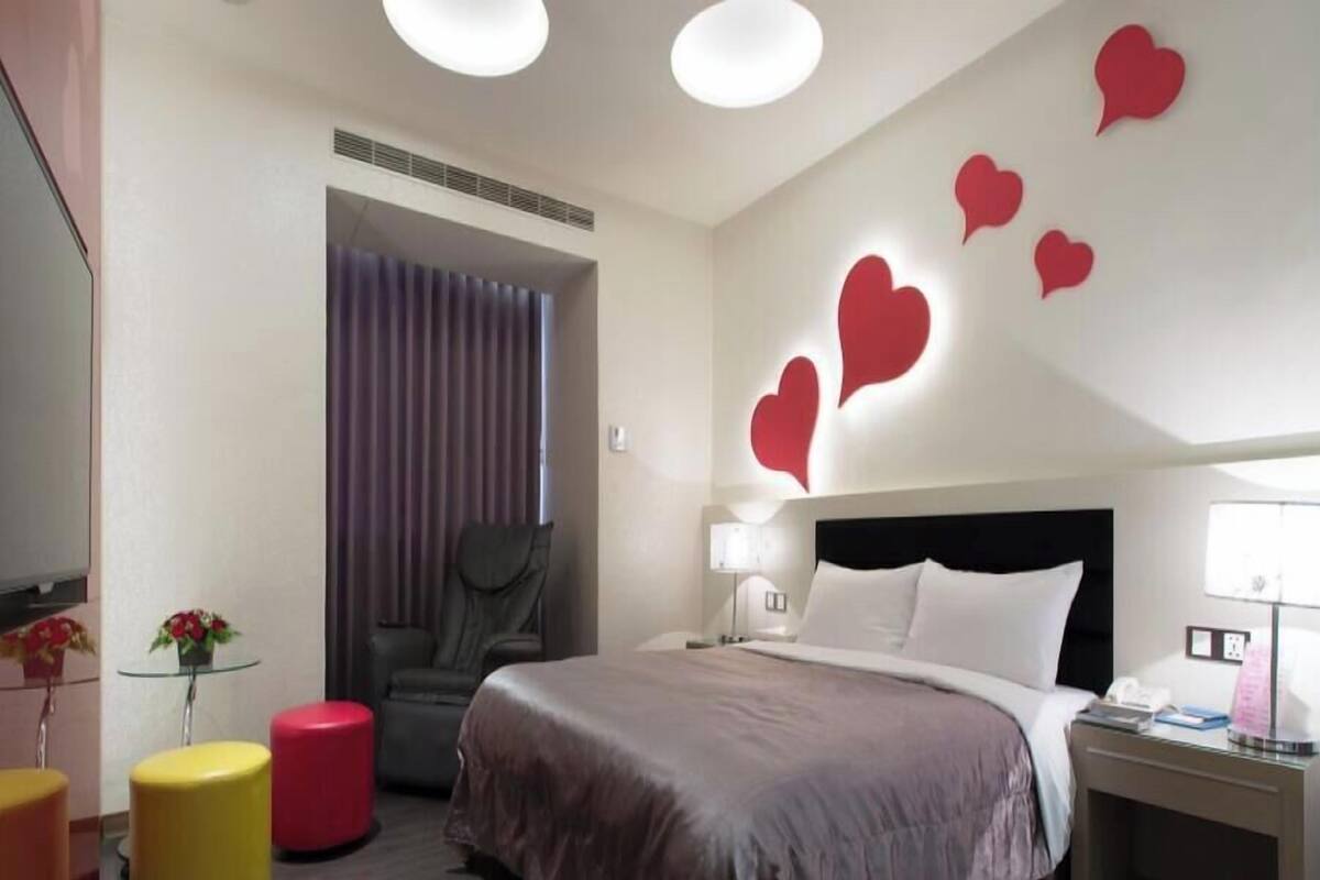Ein Hotelzimmer mit einem Bett, einem Sessel, einem Tisch mit Blumen und einer Wand mit Herzdekorationen.