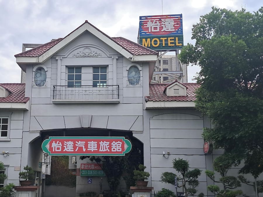 A building with a prominent sign indicating it is a motel, a large arched entrance, and a smaller sign for a car rental service.