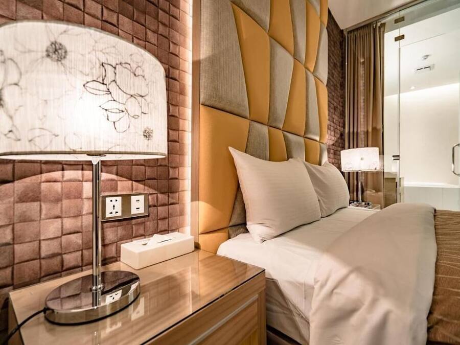 Ett hotellrum med modern design, med en säng som har ett geometriskt mönster på sänggaveln, ett sängbord med en lampa och ett vägguttag.