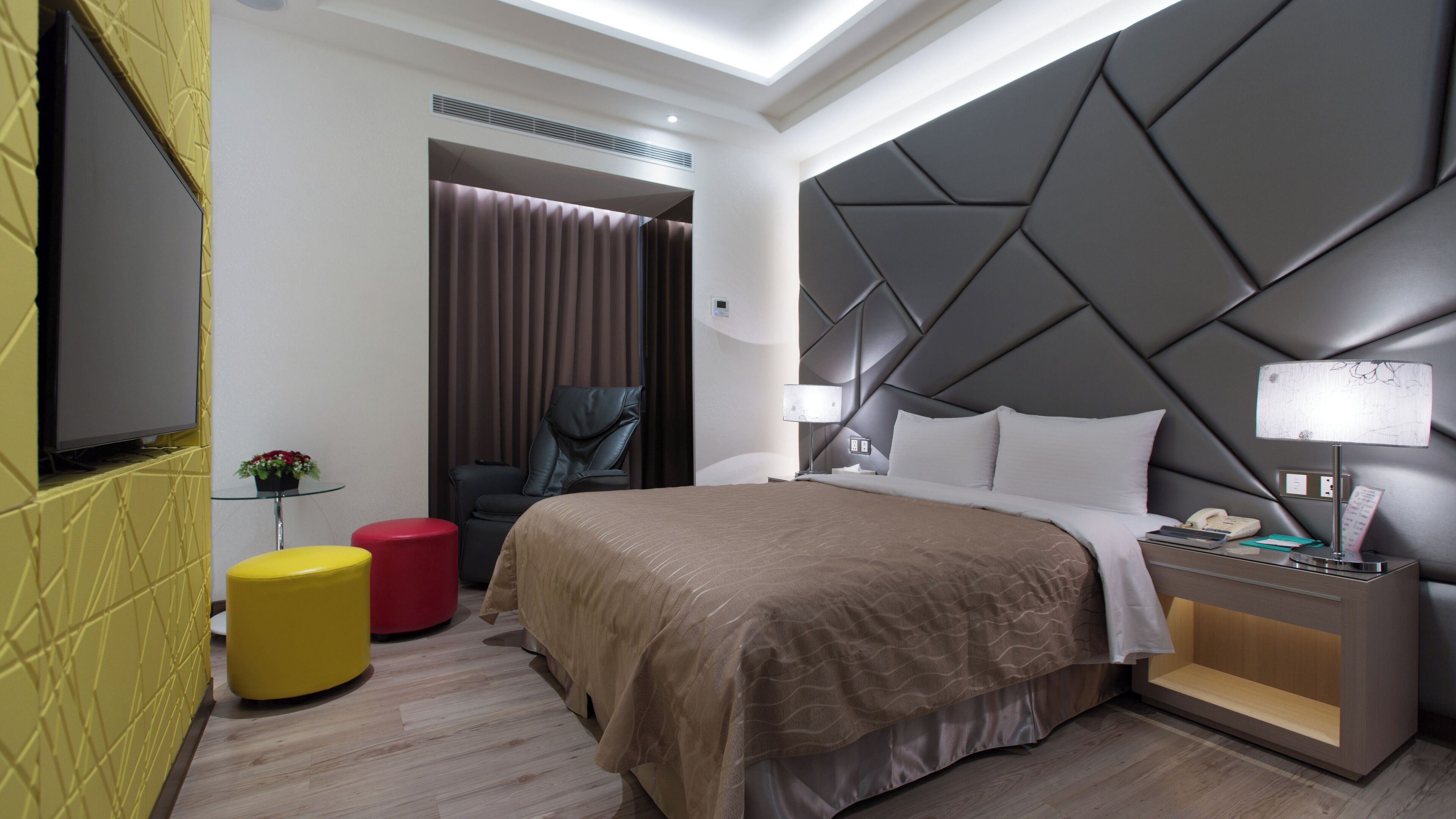 Una habitación de hotel moderna con una cama grande, un televisor, un escritorio con lámpara y una silla.