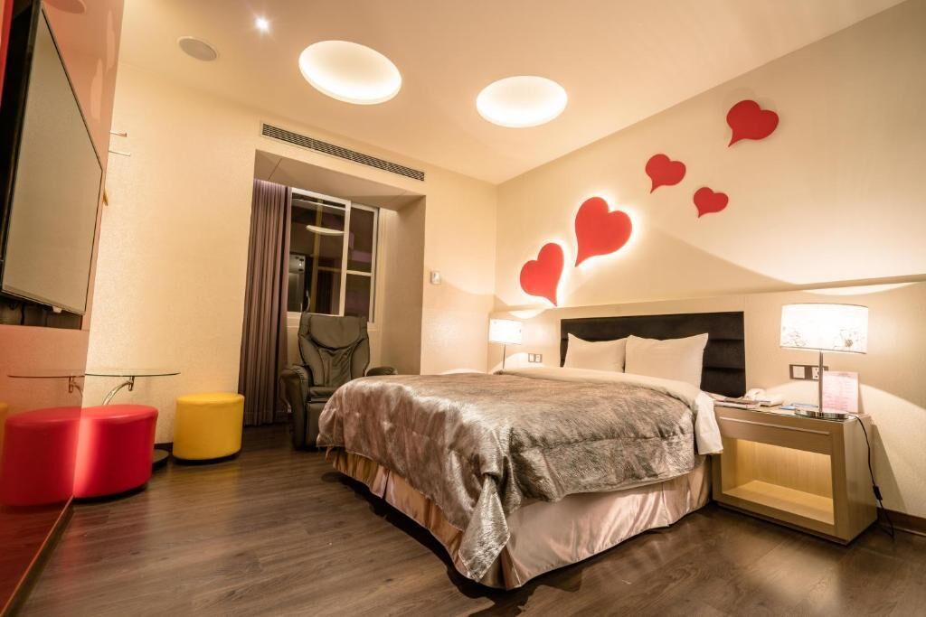 Una habitación de hotel moderna con una cama grande, mesitas de noche, un espejo y una decoración con forma de corazón rojo en la pared.
