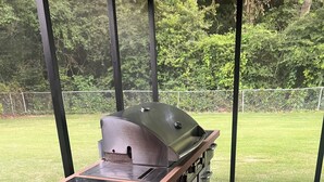 A barbecue grill with a wooden cabinet and stainless steel drawers, located in an open patio with a view of a grassy area. - 4BR 3BA • 2 Master Suites • BBQ Patio • Near Ft Benning & CSU (Columbus)