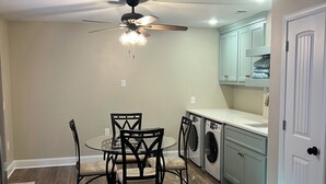 A kitchen with a ceiling fan, a dining table with chairs, a washing machine, and light blue cabinets. - 4BR 3BA • 2 Master Suites • BBQ Patio • Near Ft Benning & CSU (Columbus)