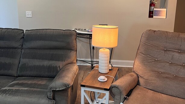 Un salon avec deux canapés, une petite table avec une lampe, une étagère fixée au mur et un extincteur.