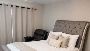 A bedroom with a large bed, a headboard, a chair, and a window with curtains. - 4BR 3BA • 2 Master Suites • BBQ Patio • Near Ft Benning & CSU (Columbus)
