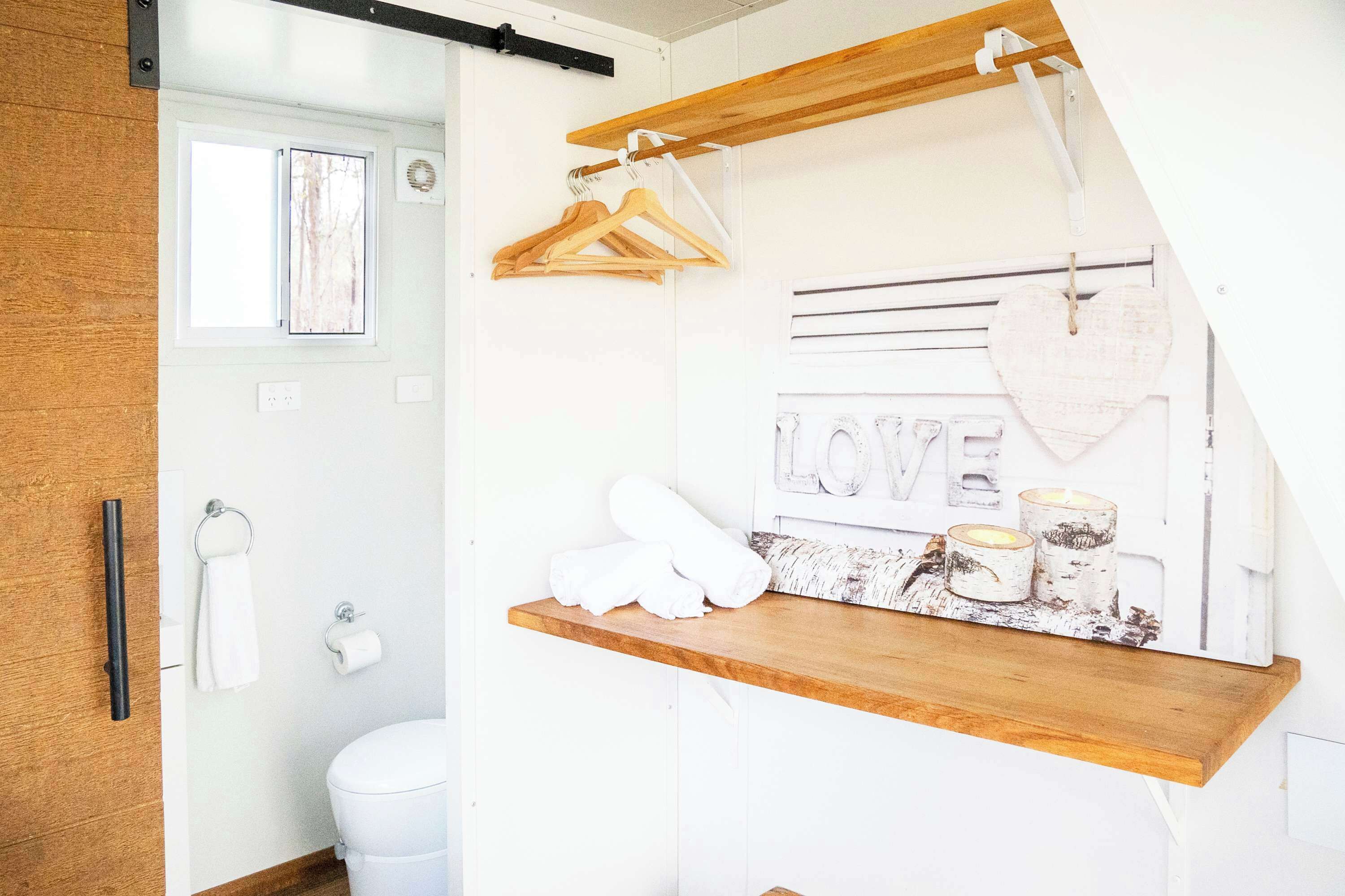 Un baño con estante de madera, toallas, inodoro y ventana.