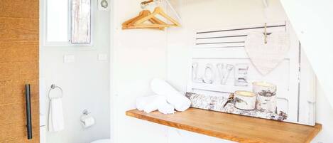 Un baño con estante de madera, toallas, inodoro y ventana.
