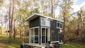A modern, two-story cabin with large glass windows, a deck, and outdoor seating.