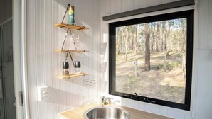A kitchen with a stainless steel sink, wooden countertop, and a window with a view of a forest.
