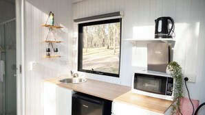 A compact kitchen with a sink, a microwave, and a coffee maker. There is a window with a view of a forest.