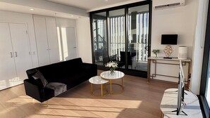 A modern living room with a black sofa, two round coffee tables, and a TV on a stand. - The Luxury Penthouse at Spring Square (Bankstown)
