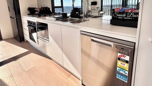 A modern kitchen with white cabinets, stainless steel appliances, and a large window offering a city view. - The Luxury Penthouse at Spring Square (Bankstown)