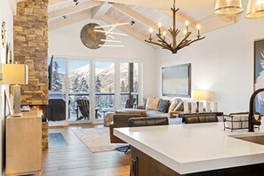 A modern kitchen with a large island, stone wall, and a view of snowy mountains through the windows.