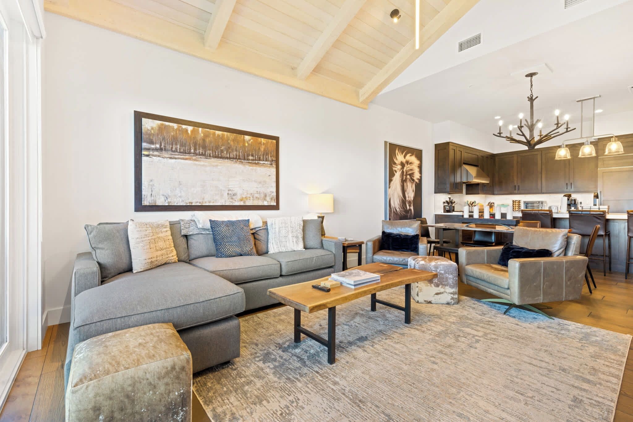 A modern living room with a sectional sofa, a coffee table, and a dining area with a kitchen in the background.