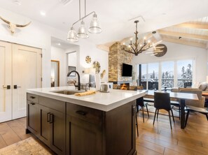 A modern kitchen with a large island, a stone fireplace, and a dining area with a view.