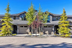 A modern two-story house with a garage, surrounded by evergreen trees and a gravel driveway.