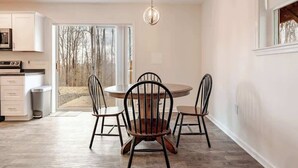 A modern kitchen with white cabinets, a dining area with a round table and four chairs, and a large sliding glass door leading to a deck.