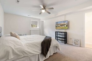 A bedroom with a bed, a ceiling fan, a TV, and a window.